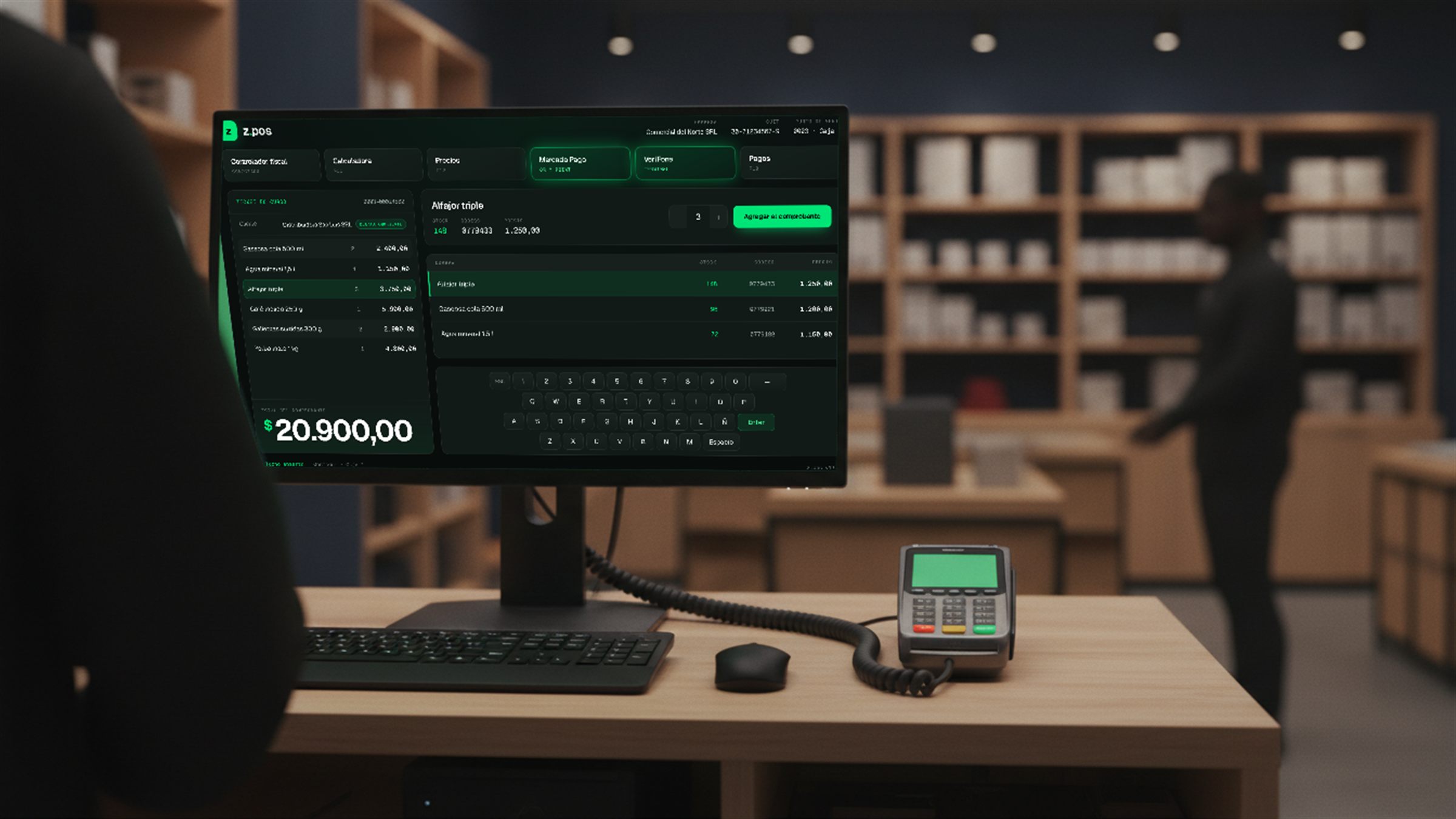 Puesto de caja de un comercio visto desde el lado del vendedor: el monitor muestra la pantalla de venta de z.pos con el total del comprobante, y un cable conecta la terminal de cobro apoyada en el mostrador con la computadora